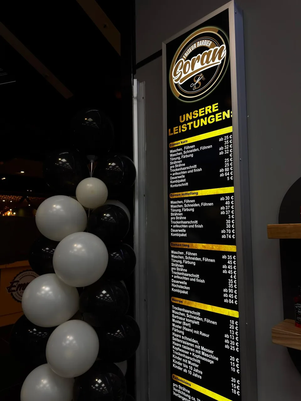 Das gold-weiße Soran-Logo auf der schwarzen Leistungstafel neben dem Saloneingang.